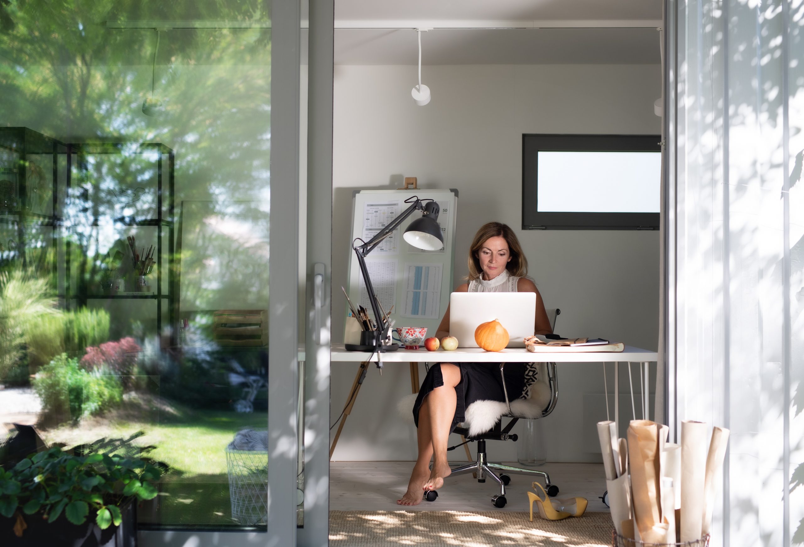 Mature woman working indoors in home office in container house in backyard.
